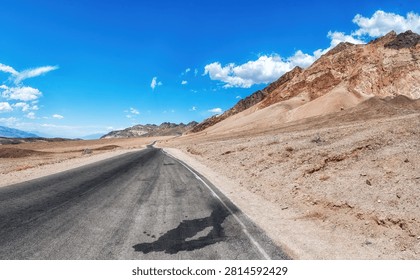 A long, empty highway stretching through the desert landscape of Death Valley, California, with distant mountains and vast blue sky, symbolizing travel, isolation, and the open road in the American West.