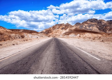 A long, empty highway stretching through the desert landscape of Death Valley, California, with distant mountains and vast blue sky, symbolizing travel, isolation, and the open road in the American West.