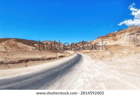 A long, empty highway stretching through the desert landscape of Death Valley, California, with distant mountains and vast blue sky, symbolizing travel, isolation, and the open road in the American West.