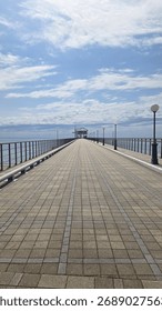 A long, empty pier extending into the sea under a blue sky with clouds.