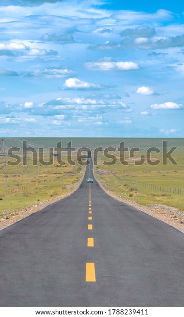A long empty road with only one green car that\
passed halfway of the road