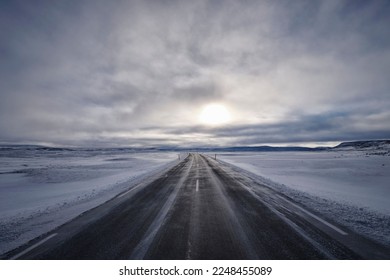 A long empty road surrounded by snow-covered fields against a cloudy day in Iceland
