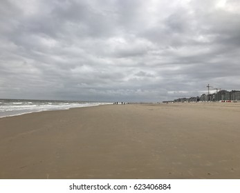 Long empty sandy beach on a cold overcast day with heavy grey clouds at a seaside resort with distant people walking and apartment blocks to the side