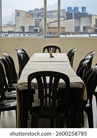A Long Empty Table with many Black Chairs and a White tablecloth