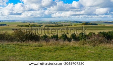 long English countryside view of green fields, woodlands and a big blue and white cloud sky seen from Sidbury Hill, Wiltshire UK