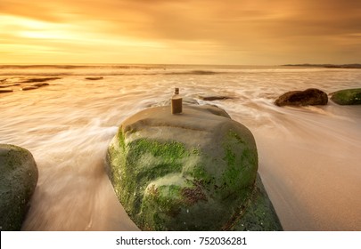 Long expose sunset with empty wiskey bottle on the rocks. image contain soft focus and blur due to long expose.
