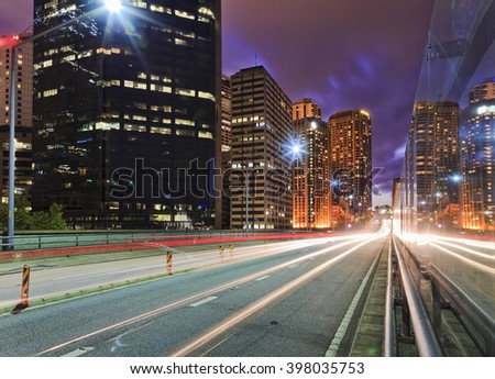 Long exposed trails of headlights and back lights of passing vehicles at sunset along high speed motorway in Sydney CBD at sunset between high-rise towers.