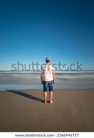 Long exposure. Beach in Brazil. Sunny and hot day on the Brazilian coast. A person standing still and the beach with the movement of the waves. Loneliness, lonely person.