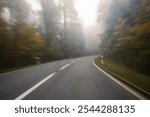 Long exposure, blurry autumn morning covered empty rural road through a forest in Europe. Wide angle view, limited visibility, bad driving weather concept, no people