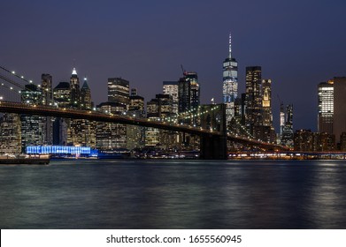 Lange Exposition von Brooklyn Bridge und Downtown Manhattan mit glattem Wasser in der Nacht