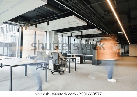 long exposure of businessman walking near colleagues working in spacious coworking environment of contemporary office, dynamic business and productivity concept