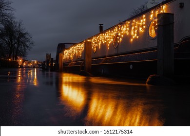 Long Exposure Of Canal Boat With Fairly Lights Moored On The River Thames In Henley On Thames With Flood Water Spilling Onto The Towpath