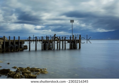 Long exposure of grieving man sitting on jetty with stormy sky, Bruny Island, Tasmania. 