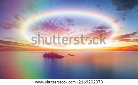 Long exposure image of dramatic sky and seascape with rock at sunset, Amazing rounded rainbow in the background 