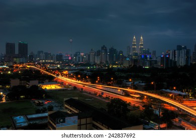 Long Exposure Of Kuala Lumpur City At Night With Light Trail Along The Highway Roads Moving And Back From The City. Visible Noise Due To Low Light, Soft Focus, Shallow DOF, Slight Motion Blur. 