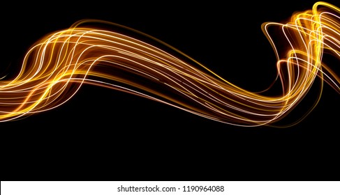 Long exposure light painting photography, curvy lines of vibrant neon metallic yellow gold against a black background - Shutterstock ID 1190964088