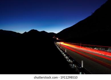 Long Exposure Of Car’s Lights On The Night Winding Road With The Silhouette Of Mountains