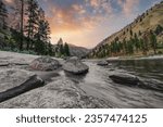 Long exposure of little salmon river in Riggins Idaho with rocks in the foreground, mountains in the background and sunset sky