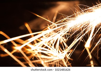 A Long Exposure Macro Shot Showing Fragments Of Burning Magnesium Falling Onto A Black Reflective Surface.