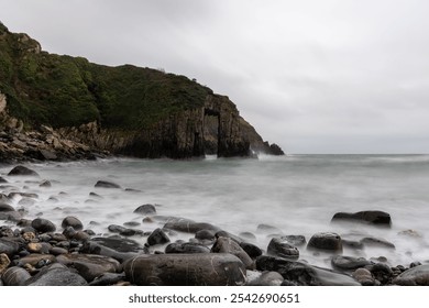 Long exposure of misty sea waves washing over rocks on beach with cliffs and natural arch in background - Powered by Shutterstock