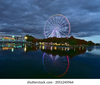 Long exposure of Montreal Grand Ferris Wheel in Old Port at the twilight blue hour. Background is cloudy moody sky. Foreground is fall color trees and reflection on Saint Lawrence (Laurent) river. - Powered by Shutterstock