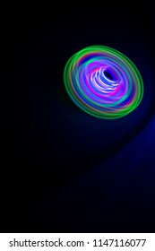 Long Exposure, Multicolor Led Light Painting Of A Spinning Top On Abstract Black Background.