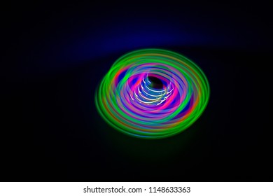 Long Exposure, Multicolor Led Light Painting Of A Spinning Top On Abstract Black Background.