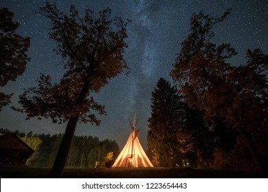 Long exposure night shot with fire lighten tipi building and Milky Way above in clear sky in Anyksciai, Lithuania