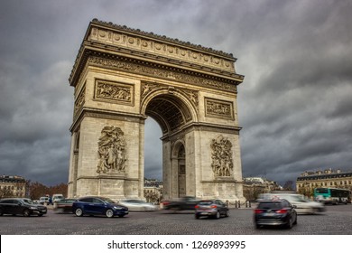 Long Exposure Photo Of The Arc De Triomphe With Ominous Clouds Overhead And Traffic Circling The Roundabout, Paris, France