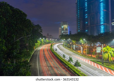 Long exposure photo of light trail from land vehicle driving through road that leads to a building and sunrise