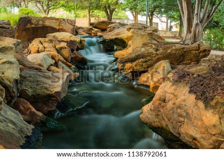 A long exposure photo of the rapids of a man-made stream and landscape in Frisco's Central Park in Texas