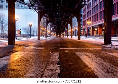 A Long Exposure Photo. Under The Train Tracks In Downtown Chicago. The Street Is Empty On This Winter Morning, And The Street Has A Bright Shine From Melted Snow.