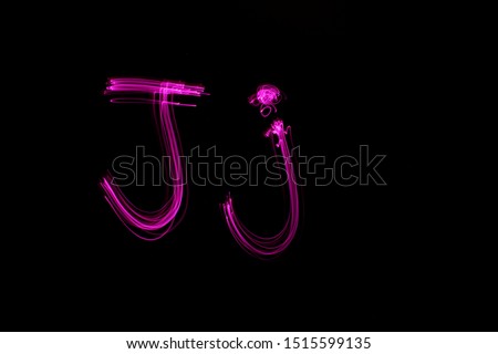 Long exposure photograph of the letter j in upper case and lower case, in pink neon colour in an abstract swirl, parallel lines pattern against a black background. Light painting photography.