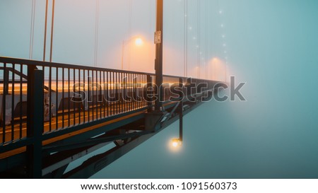 Long exposure photograph of traffic passing along a suspension bridge disappearing into the fog