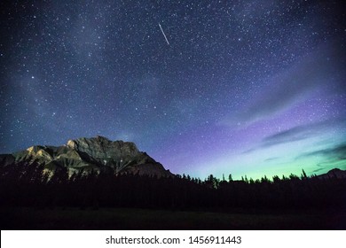 Long exposure photography of Night Sky with Northern Lights / Aurora Borealis in the distance. Photographed in Banff, Alberta, Canada.