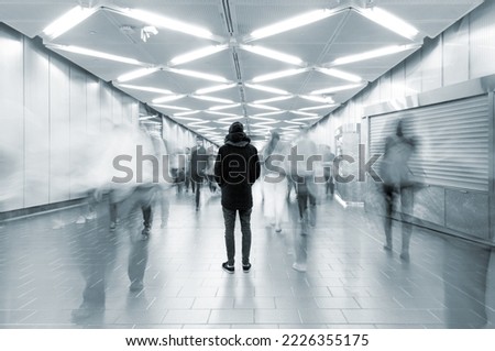 Long exposure picture with lonely man shot from behind at busy walkway with people walking in motion blur, busy city life concept