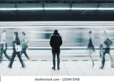 Langes Belichtungsbild mit einsamem jungen Mann, der von hinten in der U-Bahnstation mit unscharfem Zug aufgenommen wurde und die Menschen im Hintergrund