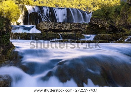 Long exposure river flow below Štrbački Buk waterfall, silky water over mossy rocks in forest canyon on the Una River, Bosnia and Herzegovina, scenic nature travel background