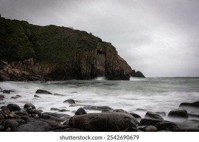 Long exposure of sea waves crashing on a rocky beach with a dramatic cliff and arch rock formation in the background - Powered by Shutterstock