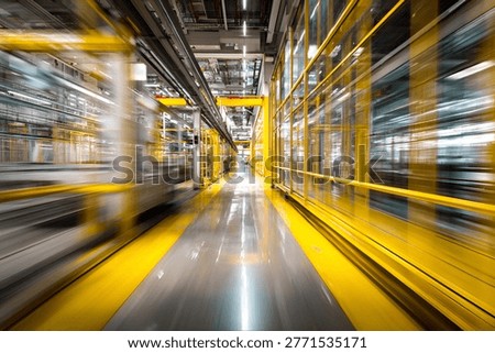 A long exposure shot captures the dynamic motion blur within a modern industrial factory hallway, featuring bright yellow safety barriers, polished concrete floors, and complex overhead piping, conve.