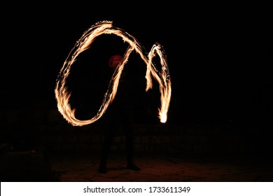 Long exposure shot from a fire juggling act, performed by a man with a red hat, showing the light trail create by the 3 burning torches. 