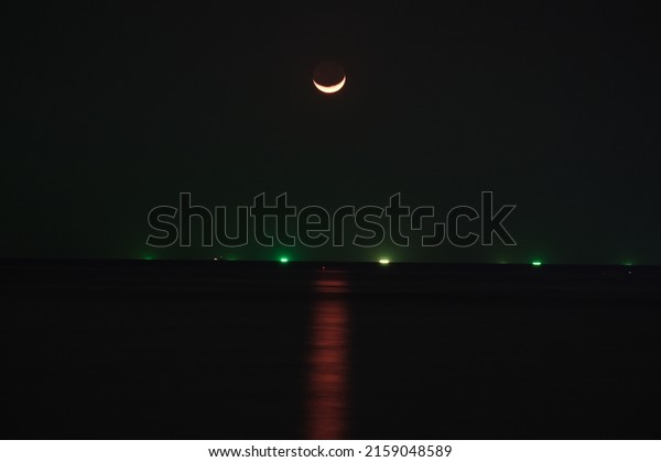 Long exposure shot of Moon above a sea, with\
moonlight path over the water is clearly visible along with lights\
of distant fishing ships
