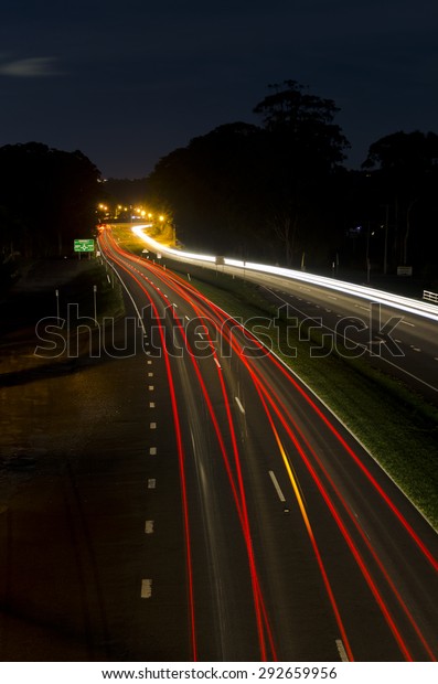 Long exposure shot at night time\
showing car headlights and tail lights as trails. One car was\
changing lane and indicator amber light can be seen on trail.\
