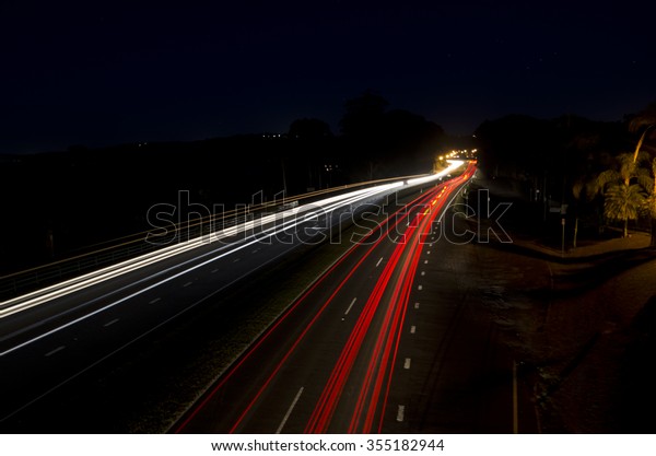 Long exposure shot at night time\
showing car headlights and tail lights as trails. Some street\
lights at a distance where the road turns. Complete dark sky.\
