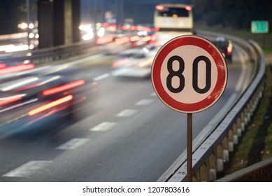 Long exposure shot of traffic sign showing 80 km/h speed limit on a highway full of cars in motion blur during the night - Powered by Shutterstock