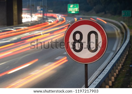 Long exposure shot of traffic sign showing 80 km/h speed limit on a highway full of cars in motion blur during the night