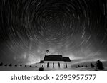 Long exposure of star trails forming circles in the night sky over a small church in winter