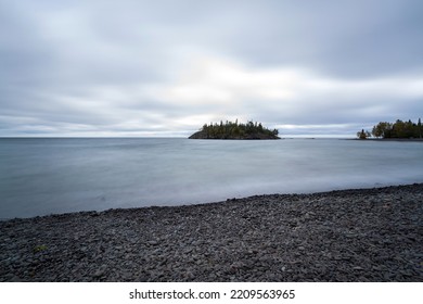 Long Exposure Of Still Water With Heavy Clouds And Island In Background