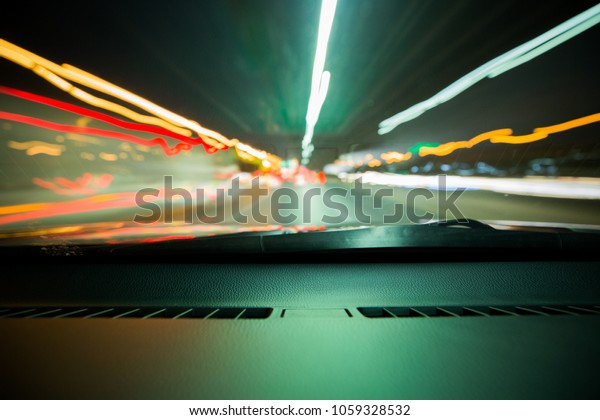 Long exposure tunnel speed of\
light inside the car. Light from the road and cars in front of the\
windshield wiper. Green temperature with orange, red, white\
light.