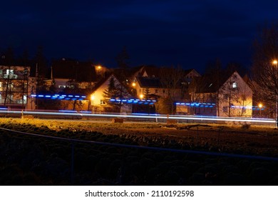 Long Exposure Of A Village At Night With Blue Light Of An Ambulance Speeding By.